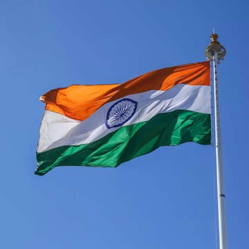 The Indian flag waves in the wind against a clear blue sky. The image symbolizes India's financial market innovation, aligning with the news about the country's first tokenized corporate bonds set to be issued in September by state-owned REC, utilizing India's central bank digital currency (CBDC) for settlement.