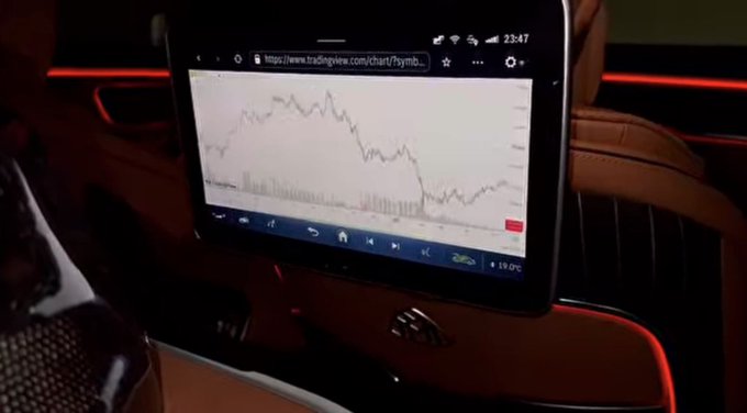 A rear-seat entertainment screen in a luxury vehicle displays a TradingView chart showing a sharply declining stock price, humorously captioned "Gn bros" to commiserate over the losses.