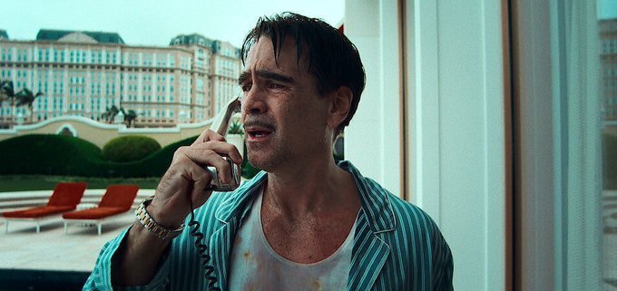 A still of a man with a mustache wearing striped pajamas talking on a corded telephone, with a large hotel building visible through the window behind him.