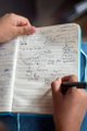 A person's hand writes notes in a lined notebook with a pen, illustrating the note-taking aspect of the "Applied Cryptography & Privacy" course taught by Adam Gibson (Waxwing/AdamISZ), the Bitcoin privacy researcher and JoinMarket co-creator featured in the post.