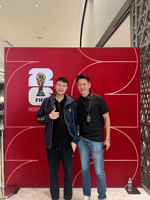 Two men pose together in front of a red backdrop displaying the 2026 FIFA World Cup logo and the word "HOSPITALITY," with the post noting they are enjoying the event as VIPs alongside Binance CEO Richard Teng.