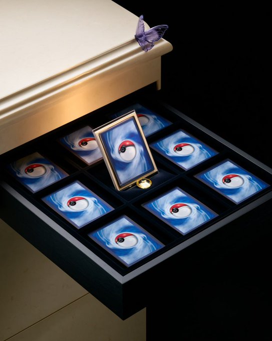 A surreal image showing an open drawer lined with Poké Balls, with one framed Poké Ball sitting upright and a purple butterfly resting on the white surface above.