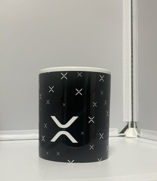 A black ceramic mug featuring white X-shaped markings and a large XRP logo design sits on a white surface.