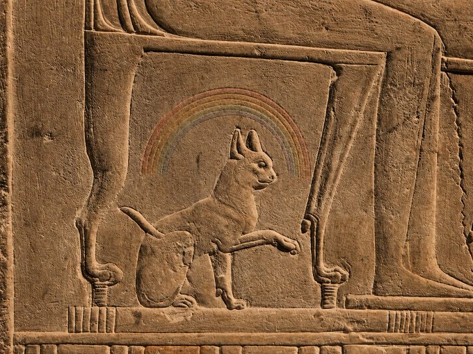 A stone relief carving depicts an ancient Egyptian-style cat beneath a multicolored rainbow, symbolizing the $COLORS memecoin. The image creatively fuses traditional Egyptian iconography with a vibrant rainbow halo to represent the "Rainbow Cat of Solana" featured in the daily post.