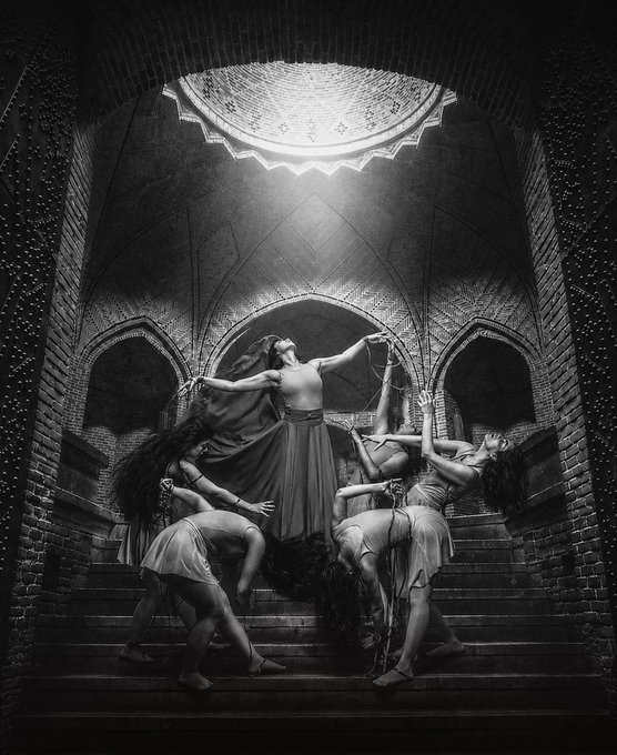 A dramatic black and white photograph identical to image 6, showing female dancers performing gracefully on stone steps beneath a lit dome.