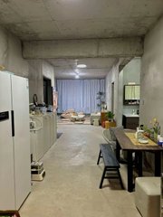 A view of a modern, minimalist apartment interior with a kitchen area on the left, a dining table with chairs, and a living space in the background.