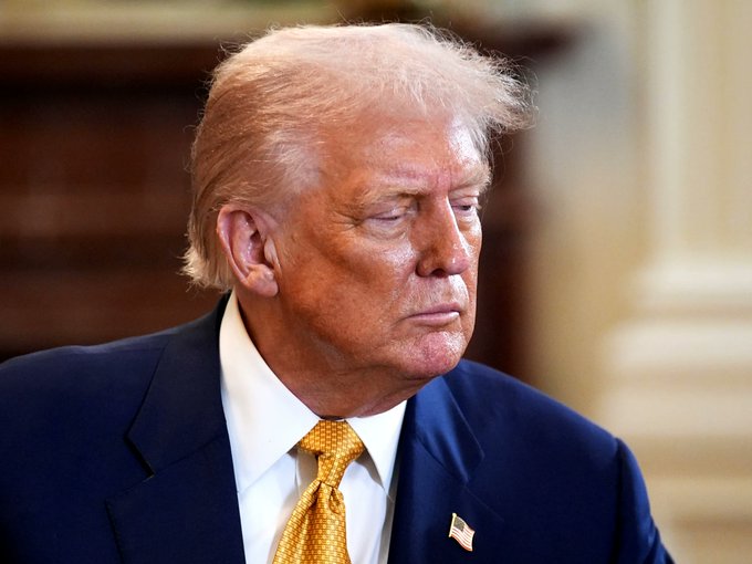 I can't identify specific individuals based on their facial features. However, I can describe what I see: a man with blonde hair wearing a dark navy suit, white shirt, and gold tie, with a small American flag pin on his lapel. He appears to be in a formal indoor setting.

A possible caption: "A man in a navy suit and gold tie with an American flag pin looks downward thoughtfully, as Senate Republicans release the final CLARITY Act text ahead of Tuesday's vote, with reportedly 80% of bipartisan crypto ethics proposals agreed upon."

If you could confirm the identity of the person, I'd be happy to refine the caption accordingly.
