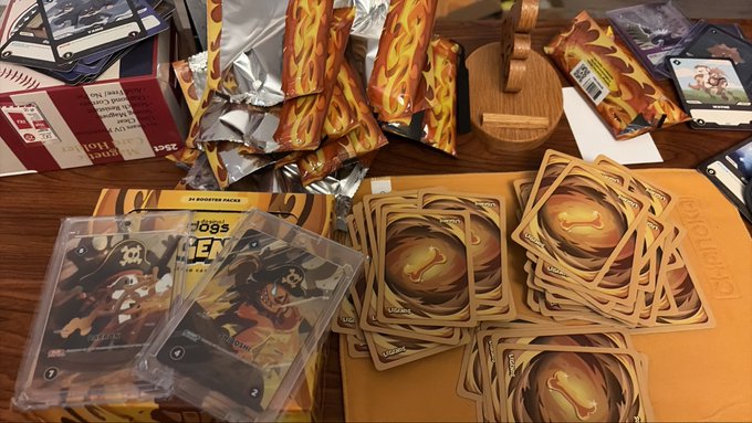 A table displaying Pokémon trading card game merchandise including a Charizard-themed booster box, blister packs, and stacked token cards.