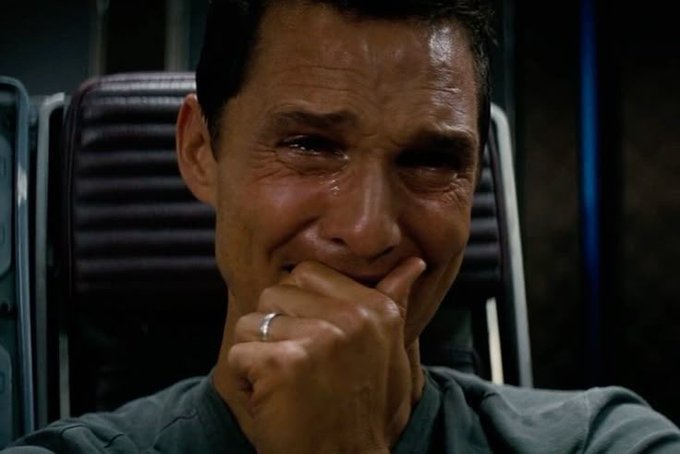 A close-up of a man with dark hair appearing to cry, covering his mouth with his hand while wearing a wedding ring, with a ring visible on his finger.