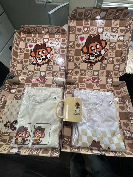 Two open 'Chimper's Cafe' gift boxes containing white t-shirts, a yellow mug, and stickers, set against a brown and beige checkered interior pattern.