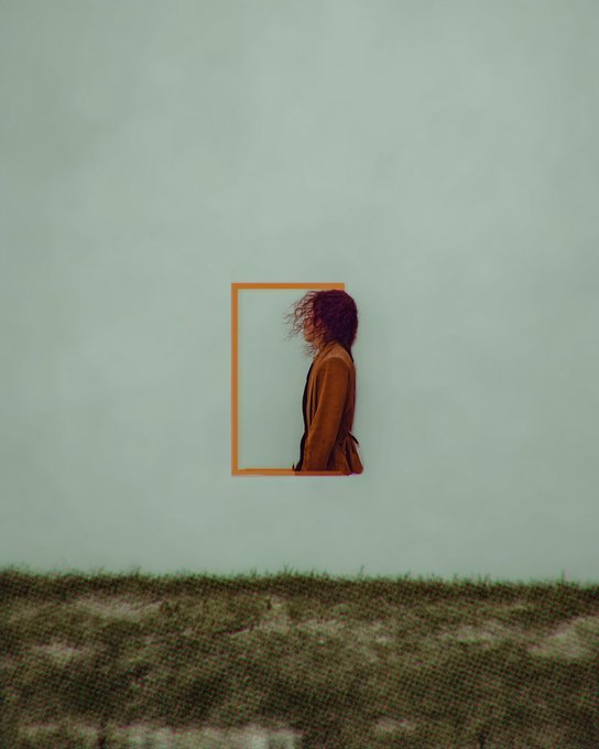 A minimalist artistic photograph showing the profile of a person with curly hair wearing a tan coat, framed by an orange rectangular outline against a large pale wall, with grassy ground in the foreground.