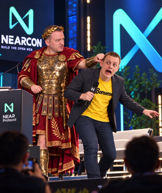 Two men appear on a conference stage: one wears a Roman-style costume and laurel crown while pointing toward a man holding a microphone and a yellow shirt reading “Borshch.” Visible branding includes “NEARCON” and “NEAR Protocol.”