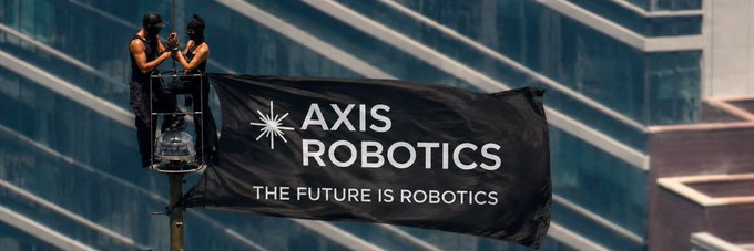 A black banner on a city building reading 'AXIS ROBOTICS - THE FUTURE IS ROBOTICS' being worked on by two people in a lift.
