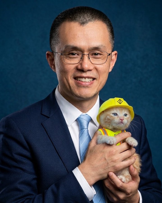The image shows a man in a navy suit holding an orange kitten wearing a yellow construction hard hat, likely referencing CZ (Changpeng Zhao), founder of Binance, given the BNB chain context. The post humorously connects CZ's well-known love of pets to the $SUE cat token on BNB chain, asking viewers to justify buying in.