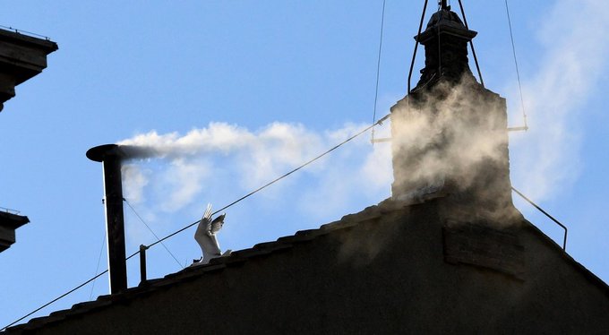 A figure in a white costume stands on a rooftop beside a smokestack emitting white smoke, reaching up toward a bell tower against a blue sky.