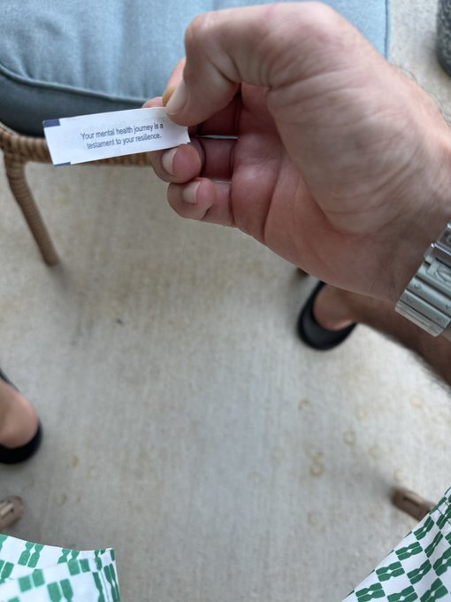 A hand holds a fortune cookie slip reading 'Your mental health journey is a testament to your resilience.'