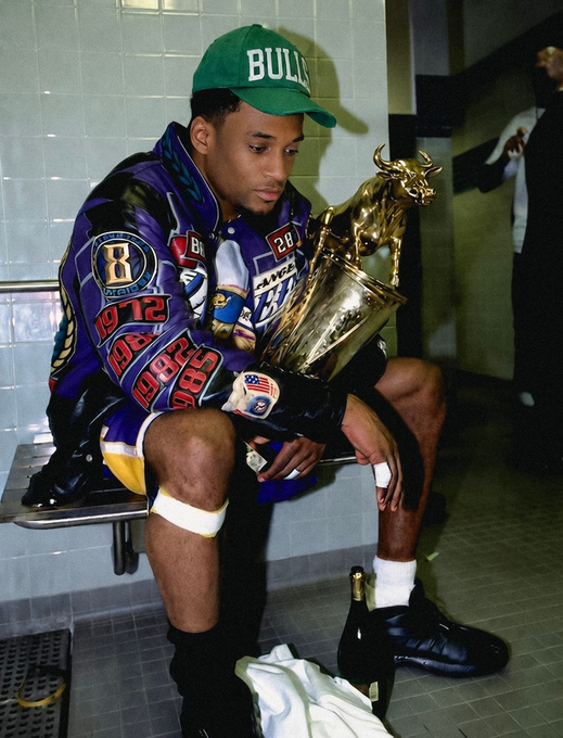 A young man wearing a green "BULLS" cap and a colorful patterned jacket sits in a locker room, holding a large gold bull trophy on his lap.
