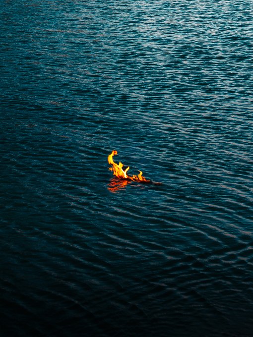 An aerial photograph showing flames burning on the surface of dark blue water.