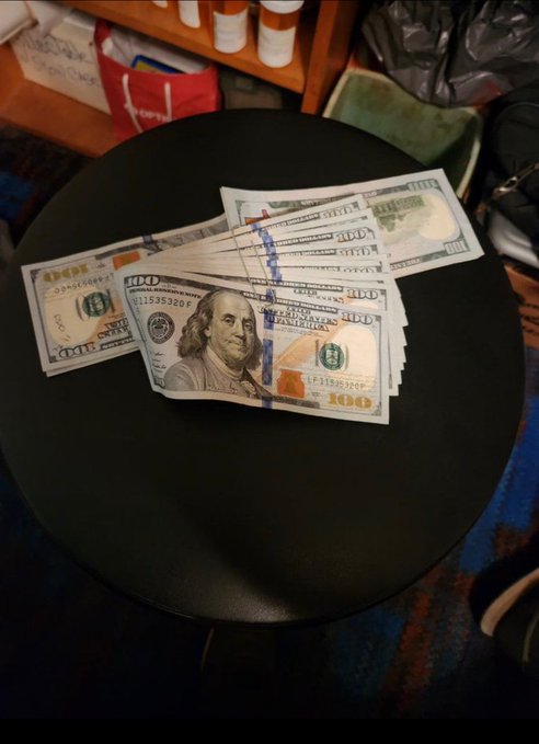 A fanned-out stack of US $100 bills with blue bank straps laid across a round black table.