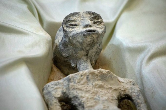 A weathered stone or clay figurine of a cat-like creature rests on cream-colored satin fabric.
