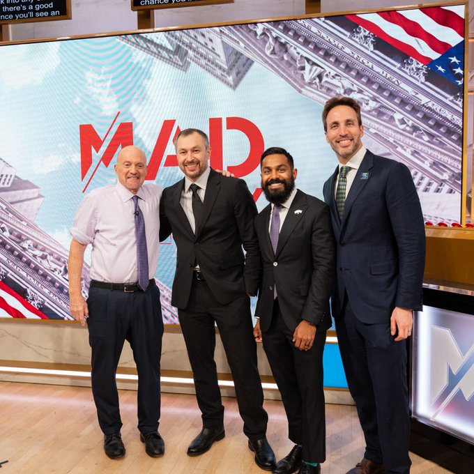 Four men in business attire posing together in a TV news studio, standing in front of a screen displaying the 'MADE' show logo with American flags.