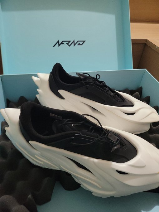 A pair of ARWA brand chunky, futuristic black and white sneakers displayed in their light blue shoebox.