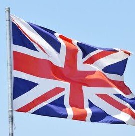 The Union Jack flag of the United Kingdom waves against a clear blue sky.