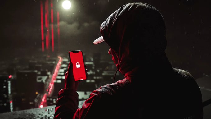 A hooded figure in a red-lit cityscape holds up a smartphone displaying a white padlock icon on a red screen.