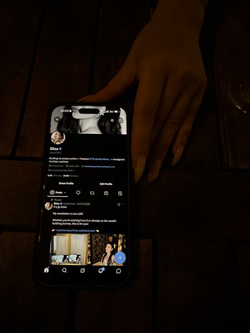 A hand resting on a wooden table beside a smartphone displaying an Instagram profile page with the username 'miamoronylne' and a blue verified badge.