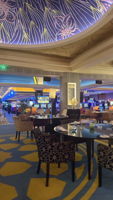 The image shows a restaurant with blue walls, yellow carpeting, and tables set up for dining. There are several chairs around each table, some of which have plates and glasses on them. The ceiling features a large design that adds an artistic touch to the space. In the background, there is a TV screen mounted on the wall, suggesting that this restaurant may also serve as a bar or entertainment venue. The post about the company's headquarters indicates that the image was taken at the company's main office in San Francisco.