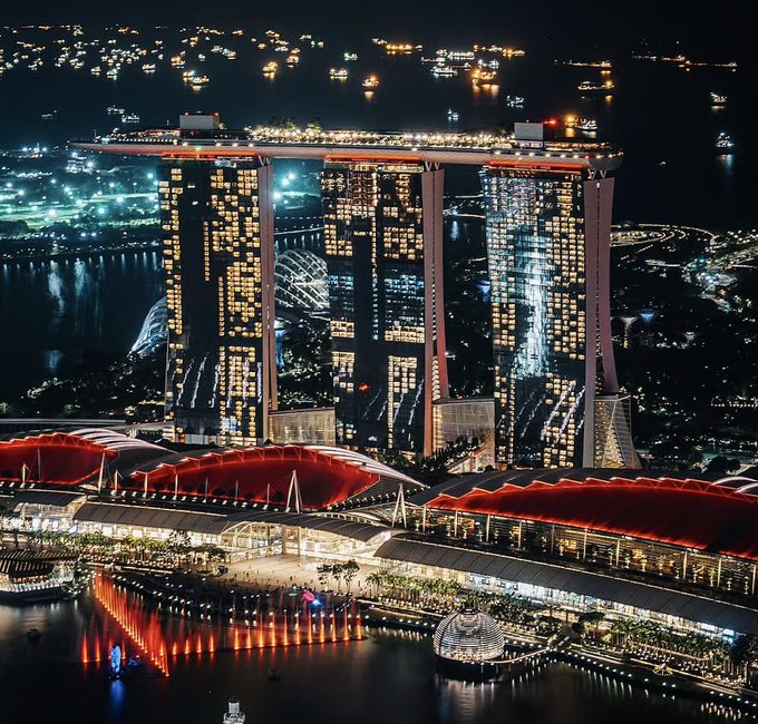 A nighttime aerial view of the Marina Bay Sands hotel and surrounding illuminated cityscape in Singapore.