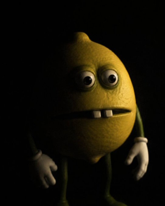 A 3D animated character resembling a yellow lemon with two large eyes, two prominent front teeth, a small green stem on top, and white-gloved hands, standing against a dark background.