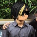 A small anime-style character with spiky black hair and yellow highlights, wearing a gray collared shirt.