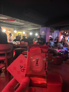 A hand holds red tickets at a FIFA World Cup venue, with a crowded, dimly lit sports bar or hospitality area in the background.