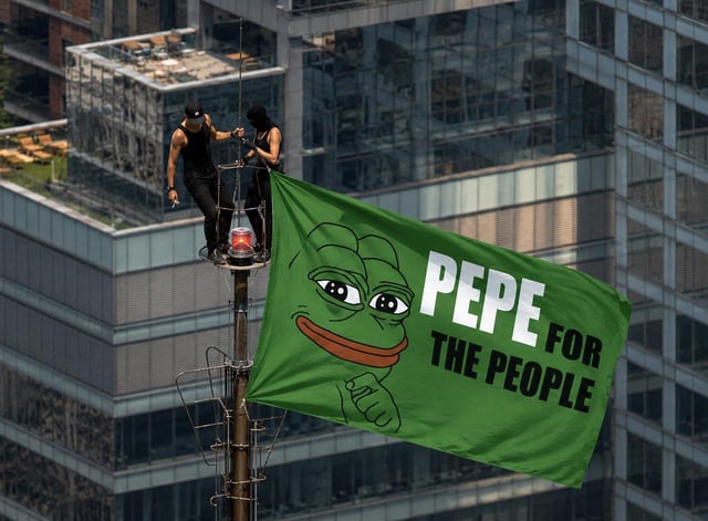 Two people atop a tall structure hanging a large green flag featuring Pepe the Frog and the text 'PEPE FOR THE PEOPLE' against an urban skyline.