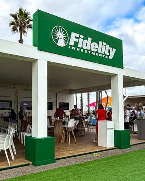 A photograph of a Fidelity Investments booth at an outdoor event, featuring a green and white branded sign with people gathered underneath.