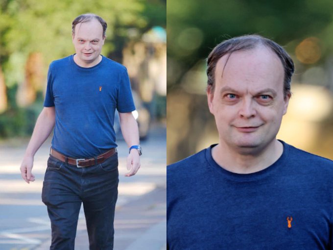 A man in a blue t-shirt with a small orange logo walks outdoors, shown in both a full-body shot and close-up portrait, seemingly hinting at a hidden crypto or stock ticker—though no specific coin name is visible in the image itself, leaving viewers to guess which one he might be holding.