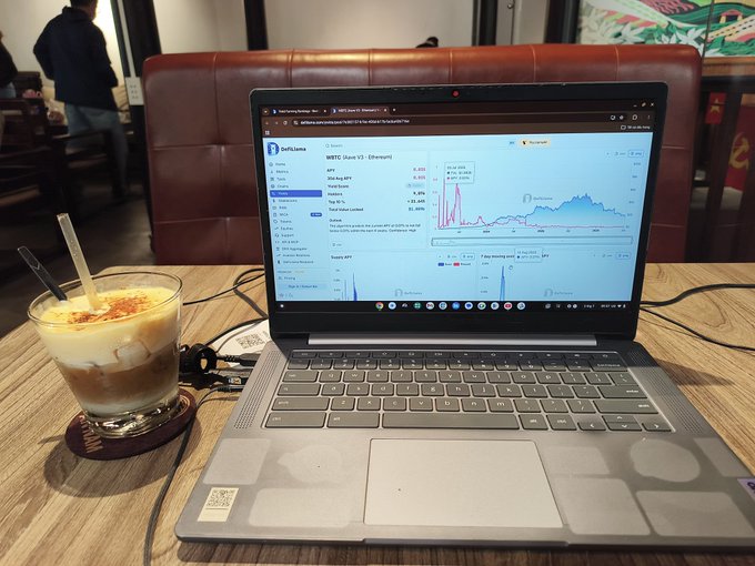 A laptop displays DeFi data for WBTC (Wrapped Bitcoin) on Ethereum, showing graphs and APY figures, as a layered drink sits beside it, seemingly relating to the crypto updates mentioned in the post.