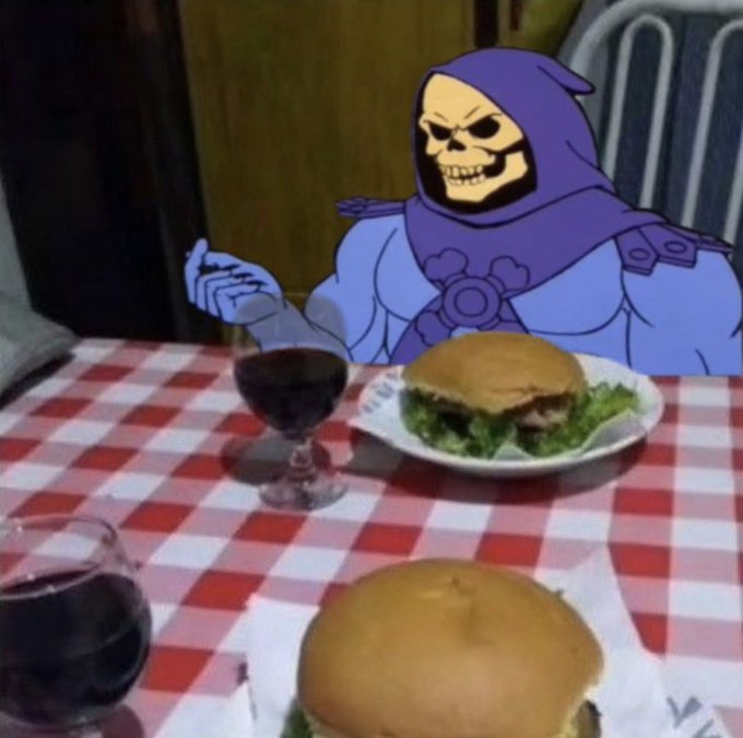 A Skeletor character from He-Man edited into a photo, sitting at a restaurant table with burgers and wine on a red-checkered tablecloth.