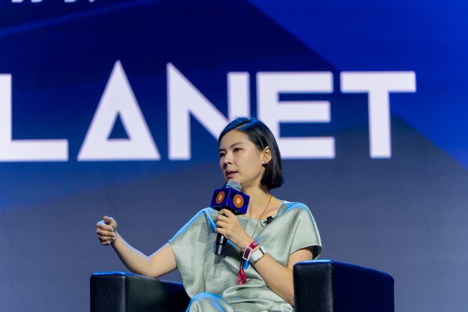 A woman with short dark hair, wearing a light green dress, speaks into a "PLANET" branded microphone while seated on stage at Bitcoin Conference Asia. The "PLANET" signage and professional setup align with the post's mention of Gracy from Bitget delivering bold, forward-looking discussions on AI, tokenization, and Bitcoin at the conference.