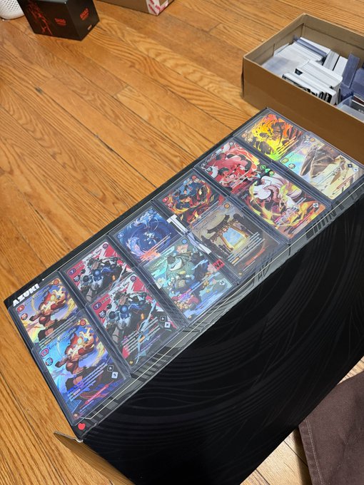 A row of Alternative Art Azuki TCG cards is displayed fanned out across an open black collector's case on a wooden floor. The visible "AZUKI" branding and holographic foil cards illustrate the rare 0.69% pulls from the case break mentioned in the post.