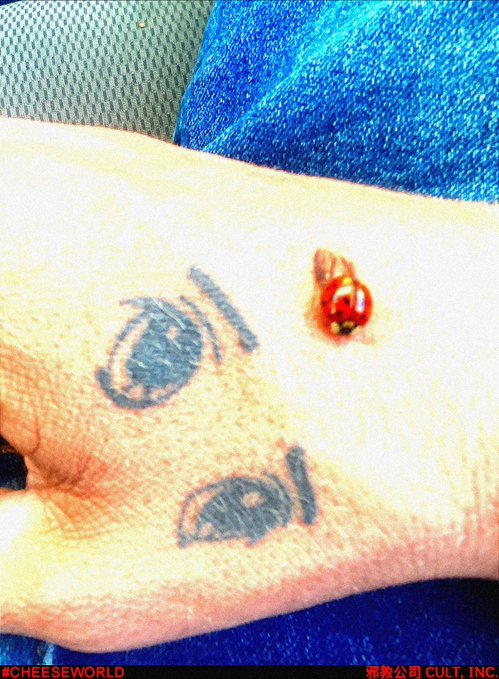 A close-up of a hand with simple line drawings tattooed on it, featuring a small 3D effect of a bleeding wound above the drawings, with watermarks '#CHEESEWORLD' and '邪教公司 CULT. INC.' at the bottom.