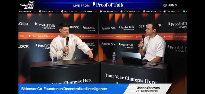The image shows a live stream of two men sitting at a table, with one man holding a microphone while the other man is wearing a white shirt. They are engaged in a discussion about AI and decentralization, as indicated by the text on the screen that reads "Your Year Changes Here". The background features a banner displaying the name "proofoftalk" along with logos for various companies such as Block and ProofOfStake.