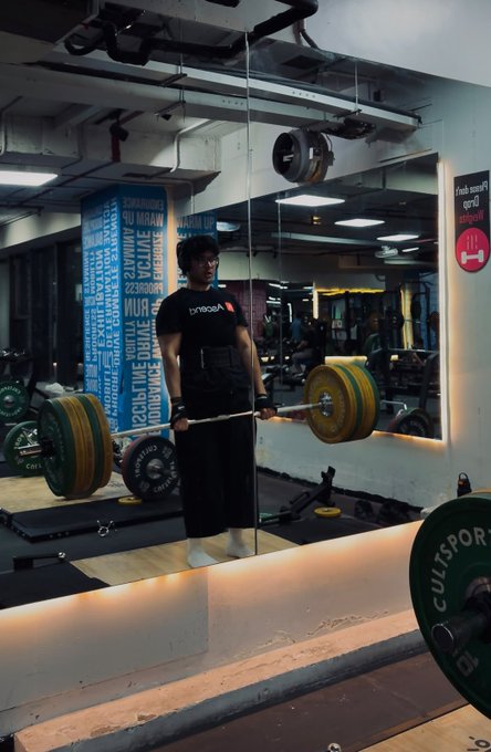 A man wearing a black "Progress" t-shirt performs a heavy deadlift with green Cultsport weight plates in a gym with inspirational wall text reading "DREAM," "EXPLORE," "EVOLVE," and "CHANGE." The image visually embodies the post's declaration of a new chapter centered on deadlifts and relentless progress.