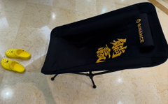 A folded black hoodie featuring traditional Chinese dragon embroidery and gold text sits on a tiled floor next to a pair of yellow Crocs.