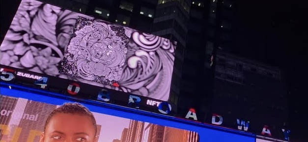 A nighttime shot of large digital billboards in what appears to be Times Square, displaying ornate floral patterns and partial text including 'ZUBAN', 'NFT', and 'BROADWAY'.