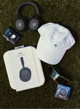 Sony branded merchandise laid out on grass, including black over-ear headphones, a white cap, Sony WF-1000XM4 earbuds box, a mouse pad, and a baseball.