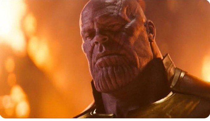 A close-up of the Marvel character Thanos, a large purple-skinned villain, set against a fiery orange background.