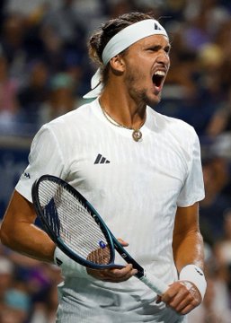 Photo of tennis player Alexander Zverev in white Adidas outfit and headband, celebrating with mouth open while holding a tennis racket.