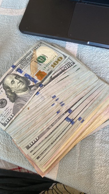 The image shows a stack of US dollar bills, including $100 bills and change, sitting on top of a bedspread or blanket. The text "All this into Brett" suggests that these bills are from the United States and might be used for financial advice.